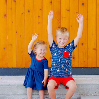 a sister and brother wearing red, white, and blue clothes put their hands in the air