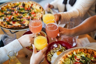 People raising a glass with pizza in the background at Rx Pizza in Bryan, Texas