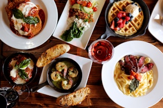 plates of shrimp, pasta, waffles, and more spread across a table at The Vintage House Restaurant in Bryan, TX