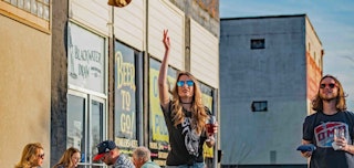 a woman enjoys a drink on a sunny restaurant patio with outdoor seating in Bryan, Texas